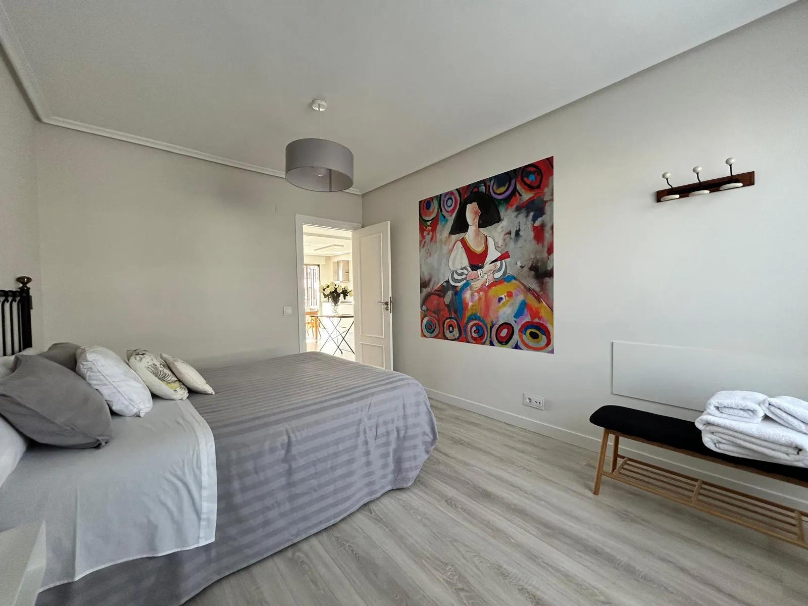Bedroom with a bench at the foot of the bed and a colourful painting